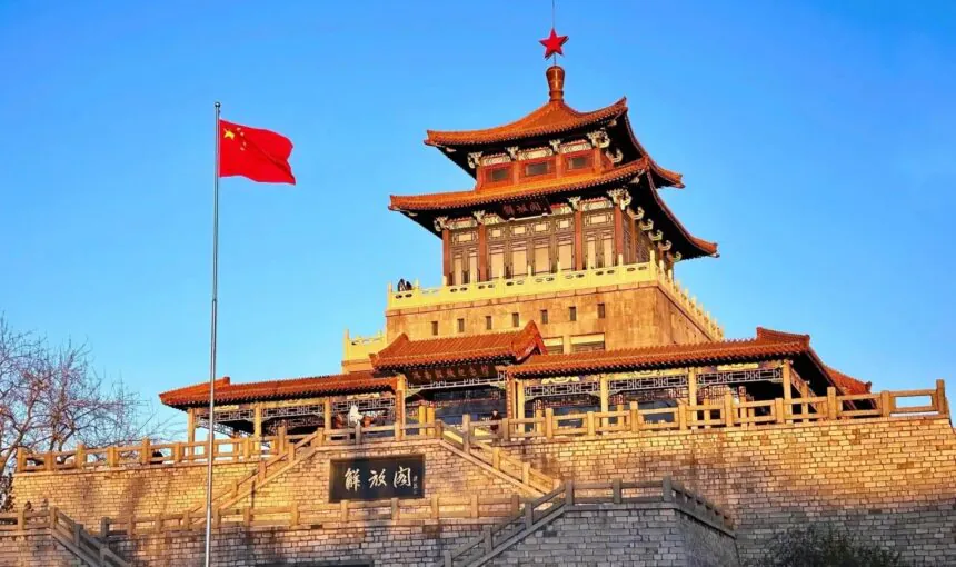 Traditional Chinese pavilion with a red flag on a pole, under a clear blue sky.