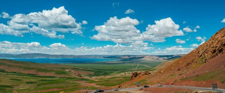 A scenic landscape of rolling green hills, a winding road, and a bright blue sky with clouds.
