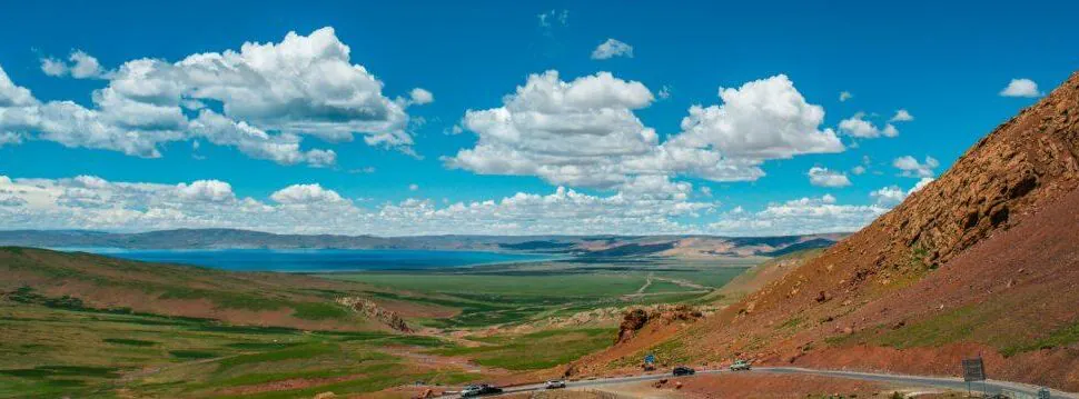 A scenic landscape of rolling green hills, a winding road, and a bright blue sky with clouds.