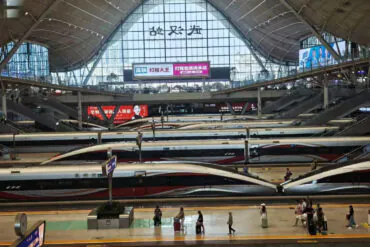 High-speed trains at a modern train station in China with a large glass roof and digital signage.