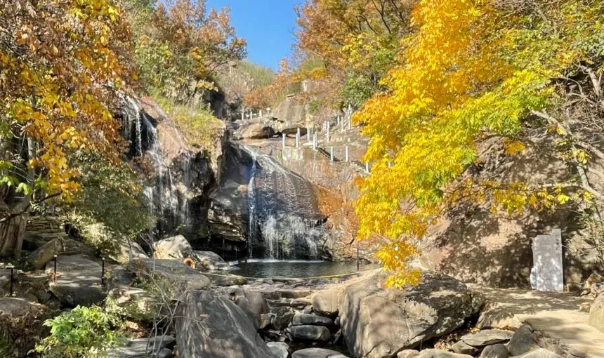 Autumn scene with waterfall, rocks, and colorful fall foliage in a natural park.