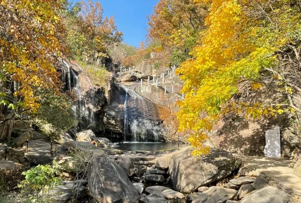 Autumn scene with waterfall, rocks, and colorful fall foliage in a natural park.
