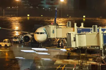 Airplane at airport gate during night with wet tarmac and airport equipment.