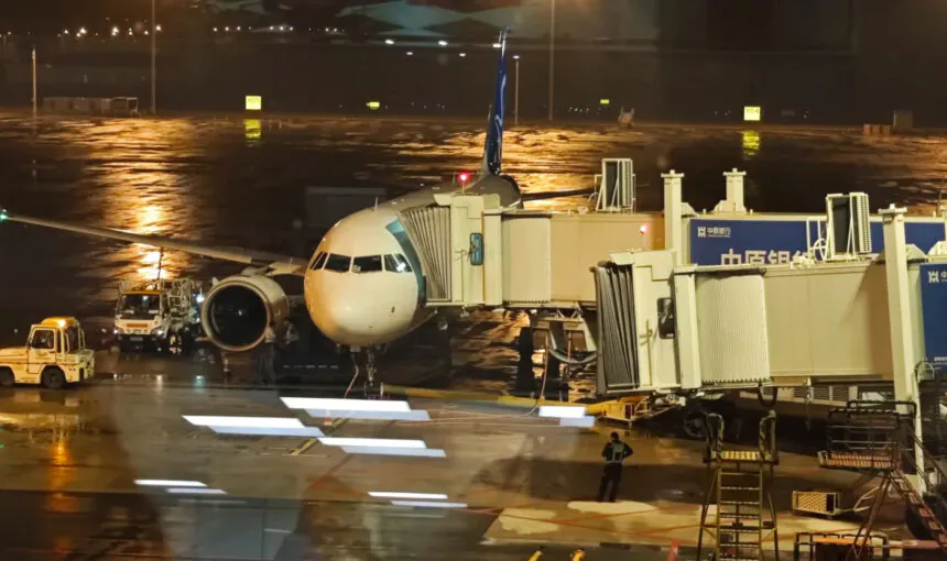 Airplane at airport gate during night with wet tarmac and airport equipment.