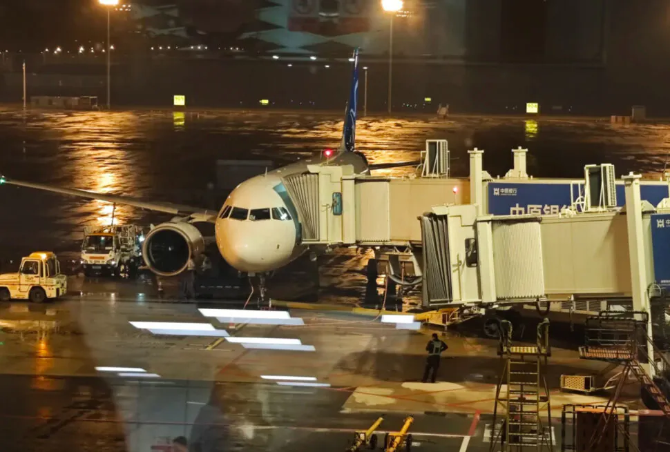 Airplane at airport gate during night with wet tarmac and airport equipment.