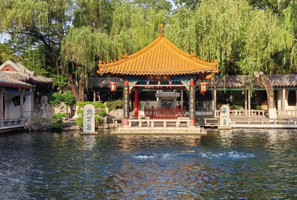 Traditional Chinese pavilion by a river with trees and lanterns.