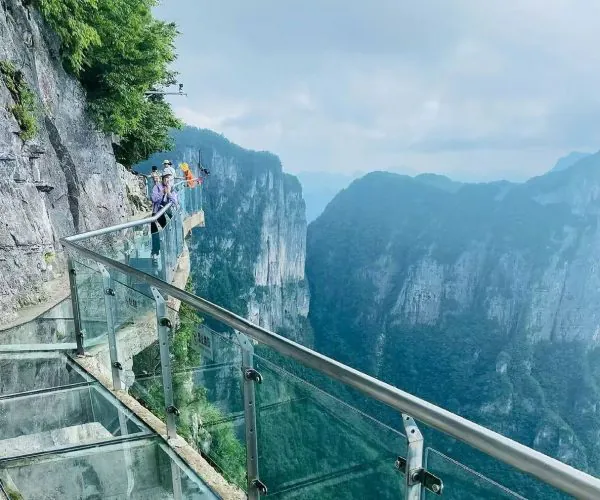 Glass walkway along a steep cliff edge with visitors looking out over a deep canyon.