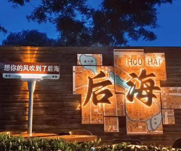 Night scene of a wooden wall with an illuminated map-marts art piece featuring large glowing Chinese characters, against a dark blue evening sky. or Wooden wall installation with a lit multi-panel map and big illuminated Chinese characters, in a nighttime setting.