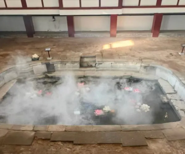 Huaqing Hot Springs and Ancient Baths,X`an,Chinatour Indoor stone pool steaming with floating flowers, set in a room with red pillars and a wooden railing above.