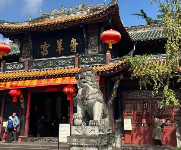 Traditional Chinese temple exterior with ornate roof, red lanterns, and a stone guardian lion at the entrance.