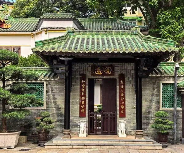 Traditional Chinese gate with a green tiled roof and red couplets, opening to a small courtyard garden.