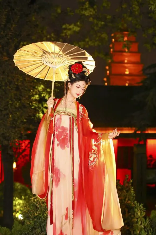 Hanfu photoshoot, xingqing palace, xi'an, solo, tang dynasty, female, chinatravel, Woman in a red and pink traditional Chinese hanfu, holding a paper parasol, posing gracefully at night with illuminated lanterns in the background.