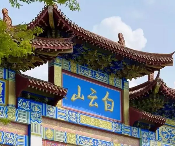 Ornate Chinese temple gate with blue plaque and gold characters, colorful painted beams, and curved tiled roofs.