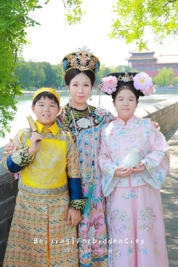 hanfu photoshoot, the forbidden city, beijing, qing dynasty, family, chinatrip, Three people in ornate traditional Chinese attire posing together outdoors by a river and temple buildings in the background.