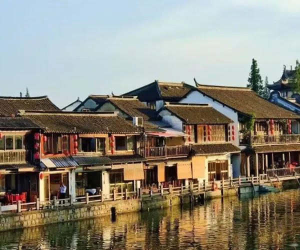 Traditional riverside street of two-story wooden buildings with tiled roofs, red lanterns, and balconies along a calm canal.