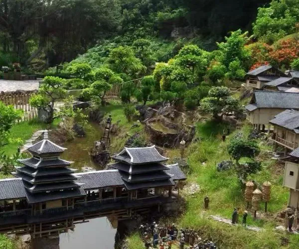 Miniature traditional Asian village with tiered pagoda buildings, a wooden bridge, and lush garden scenery.