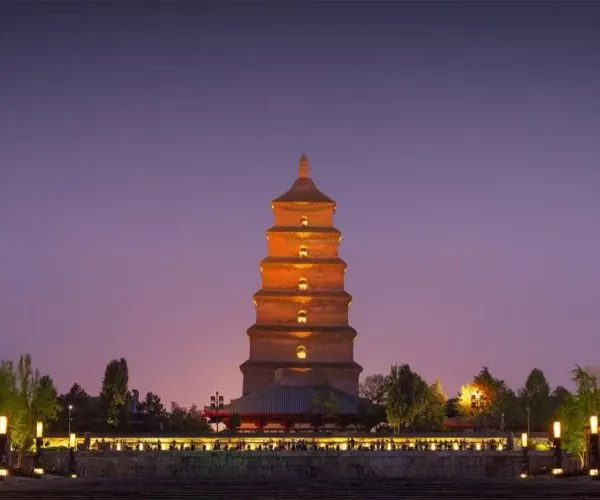 Wild Goose Pagoda and North Square,Xi`an,Chinatour Five-story brick pagoda glowing orange at night, surrounded by trees and a lantern-lit plaza.