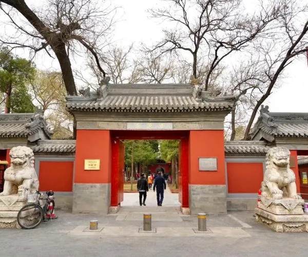 Tanzhe Temple, beijing, chinatravel, Red ceremonial gate with stone guardian lions at the entrance of a temple/park, people walking through amid bare trees.