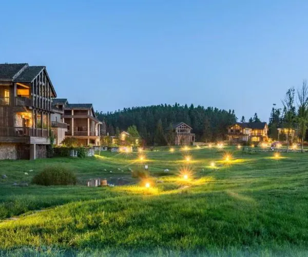 Row of wooden cottages on a glowing green lawn with warm ground lights at dusk in a resort setting
