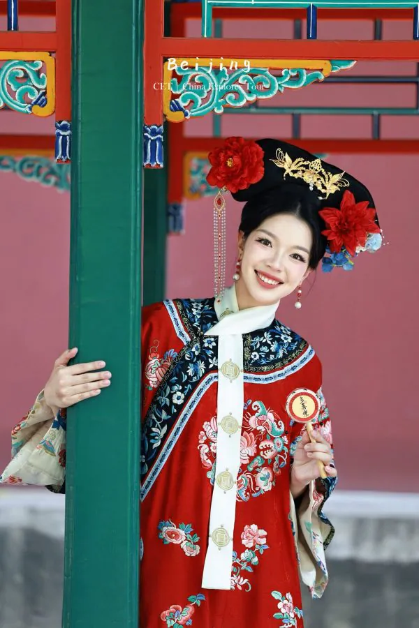 hanfu photoshoot, the forbidden city, beijing, qing dynasty, female, solo, chinatravel, Smiling woman in a red and blue ornate traditional Chinese dress with a floral headdress, posing beside a green pillar, Bejing text overlay in the background