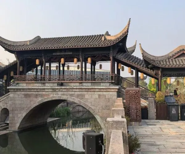 Cao'e River Pedestrian Street ,Shaoxing,Chinatour Traditional Chinese covered bridge with curved tiled roofs and hanging lanterns over a stone arch spanning a calm canal/river