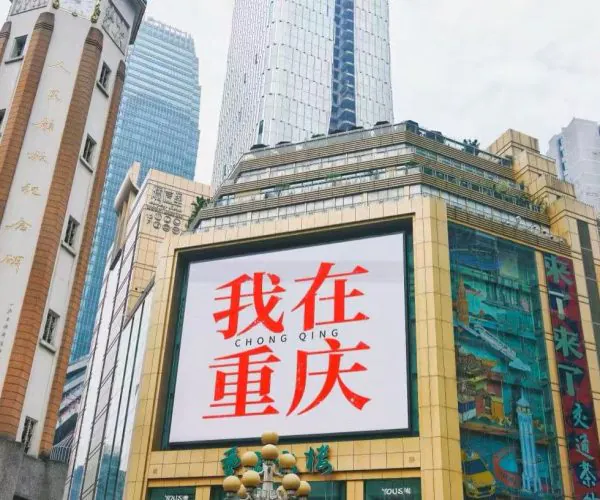 Large billboard on a gold-framed building in Chongqing displaying red Chinese text '我在重庆' (I'm in Chongqing).