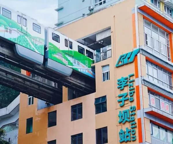 Elevated green-and-white train gliding on a monorail above a peach-colored building with turquoise signage in Chinese characters