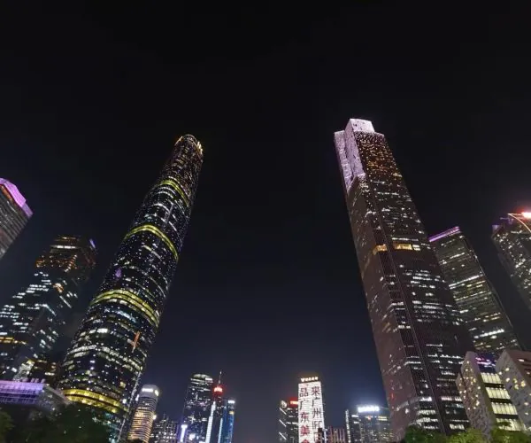 Nighttime city skyline with tall, illuminated skyscrapers against a dark sky, colorful building lights creating a vibrant urban vista