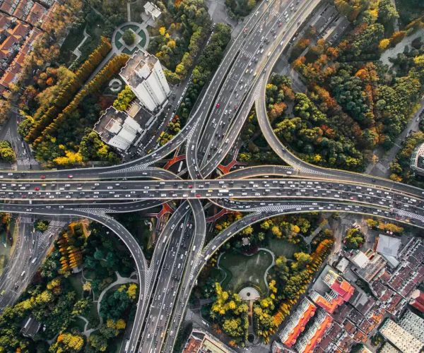 transportation, Chengdu, Chinatravel, Aerial view of an intricate urban highway interchange with looping ramps and heavy traffic, surrounded by autumn-colored trees while buildings line the edges.