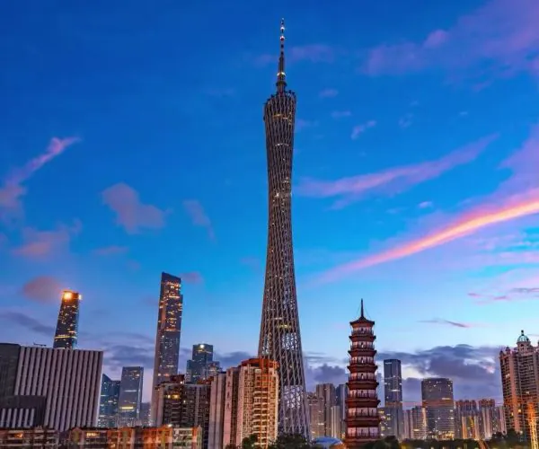 Evening city skyline with a tall twisted tower and a pagoda-style building in the foreground against a blue sky.