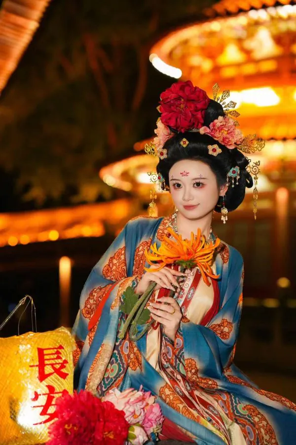 Hanfu photoshoot, xingqing palace, xi'an, solo, tang dynasty, female, chinatravel, Chinese opera performer in an ornate headdress and blue robe, holding orange flowers against a lantern-lit night backdrop.