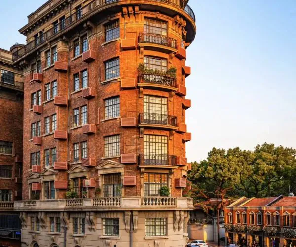 Corner brick residential building with curved corner and multiple balconies on a busy city street at sunset.