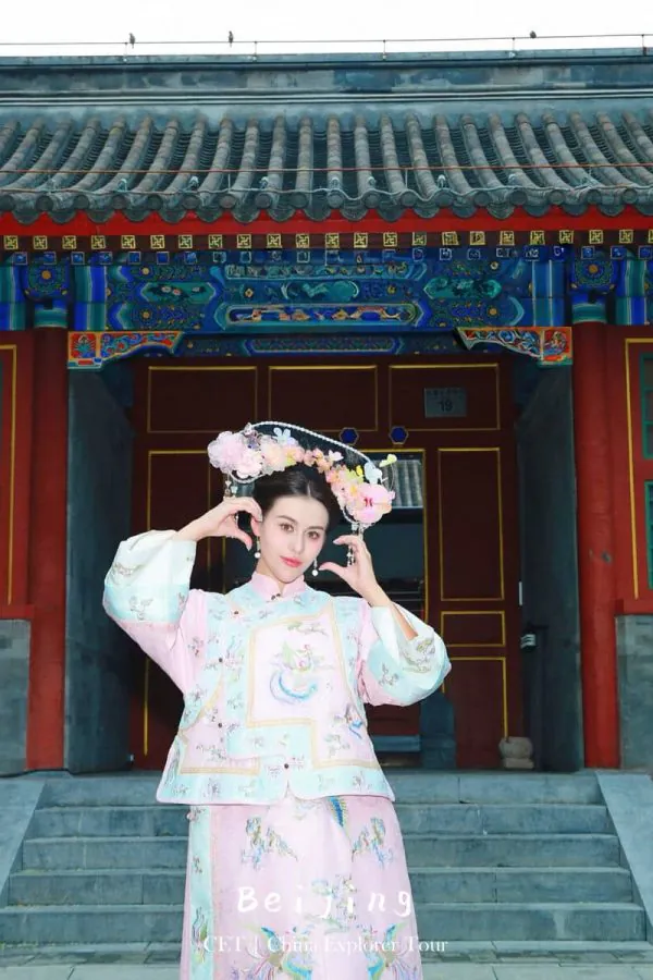 hanfu photoshoot, the forbidden city, beijing, qing dynasty, female, solo, chinatravel, Woman in a pastel pink traditional Chinese dress with a floral headdress posing on the steps of a colorful temple with blue and red architectural details.