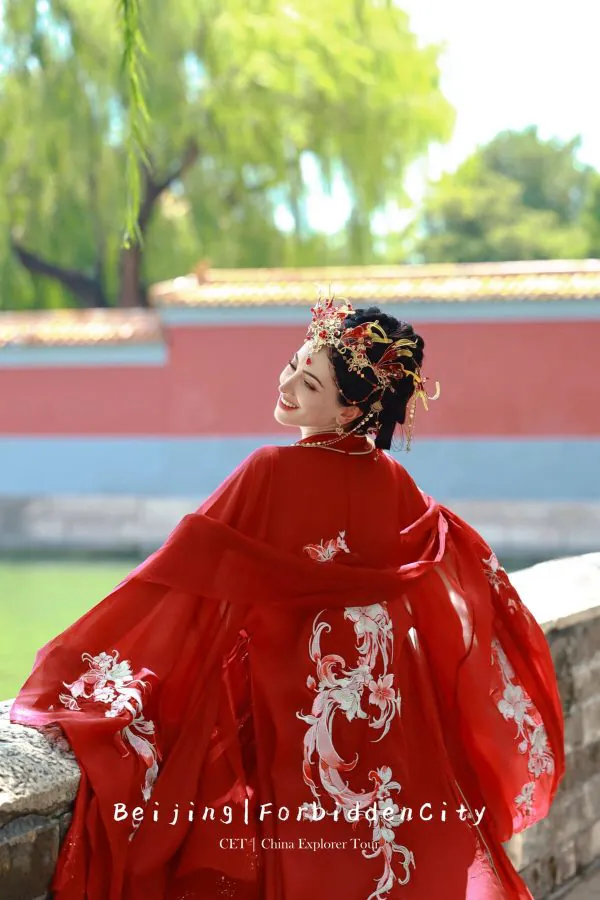 Hanfu photoshoot, the forbidden city, beijing, solo, chinatravel, Smiling woman in a red, embroidered traditional gown with an ornate gold headpiece, outdoors by a stone railing in Beijing (Forbidden City) on a tour poster.