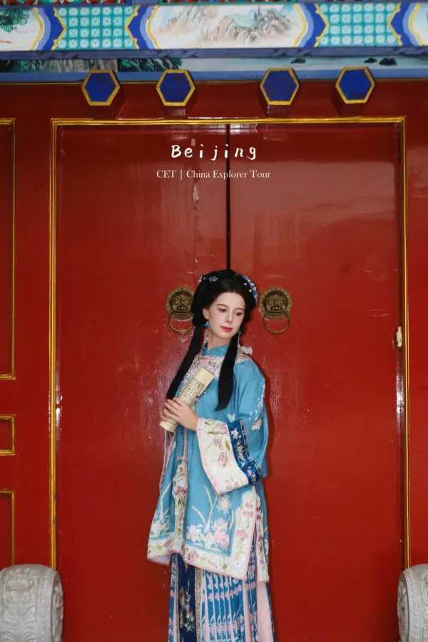 hanfu photoshoot, the forbidden city, beijing, qing dynasty, female, solo, chinatravel, Woman in blue traditional Qing-dynasty dress holding a scroll, standing before a large red ornate door with blue hexagonal accents (Beijing, CET | China Explorer Tour).