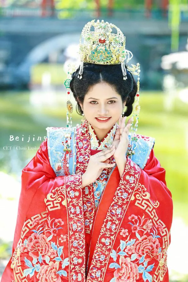 Hanfu photoshoot, zhongshan park, beijing, chinatravel, Woman wearing an ornate gold headdress and red embroidered traditional Chinese ceremonial dress, posing outdoors with a gentle smile.