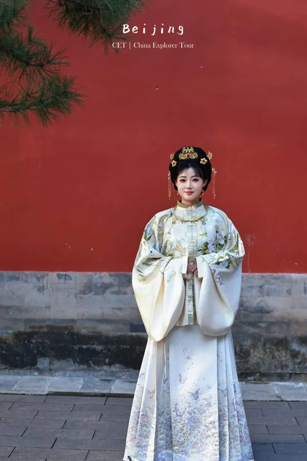 Hanfu photoshoot, the forbidden city, beijing, chinatravel, Woman in a traditional ornate Hanfu dress with a gold headdress stands before a red wall, hands in front in a calm gesture