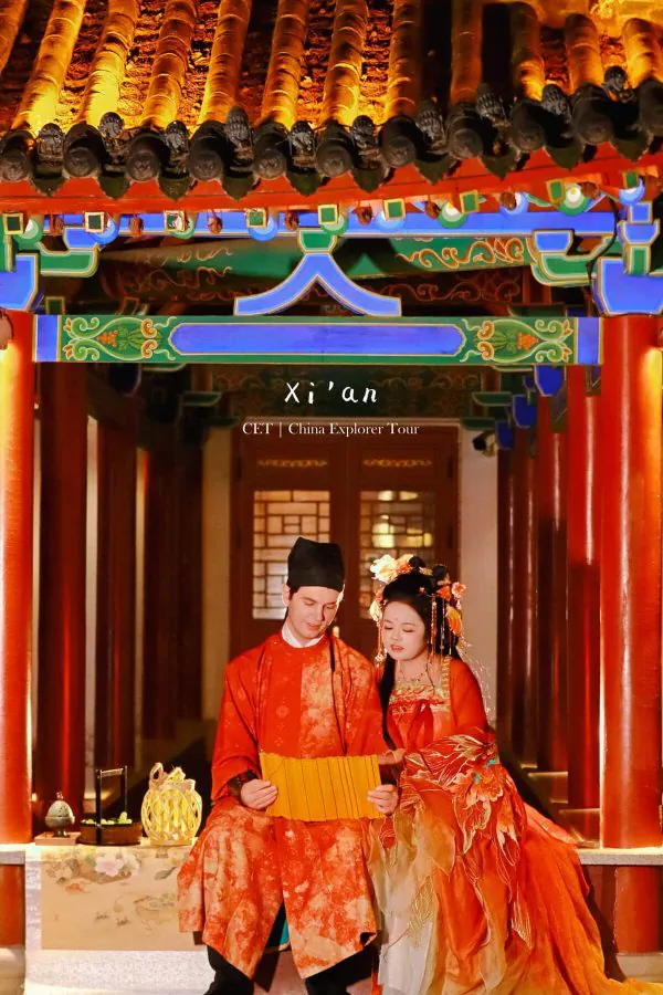 Hanfu photoshoot, xi'an, xingqing palace couple, chinatravel, Couple in red traditional Chinese wedding attire standing in a colorful temple doorway.