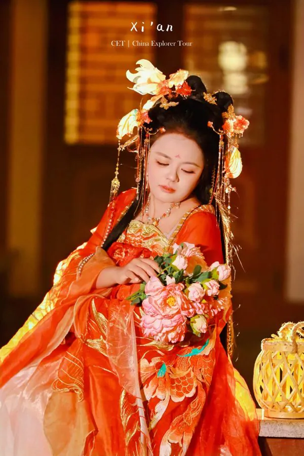 Hanfu photoshoot, zhongshan park, beijing, solo, tang dynasty, female, chinatravel, Woman in ornate red and orange traditional Chinese dress with a floral headdress, gazing at a pink bouquet she holds.