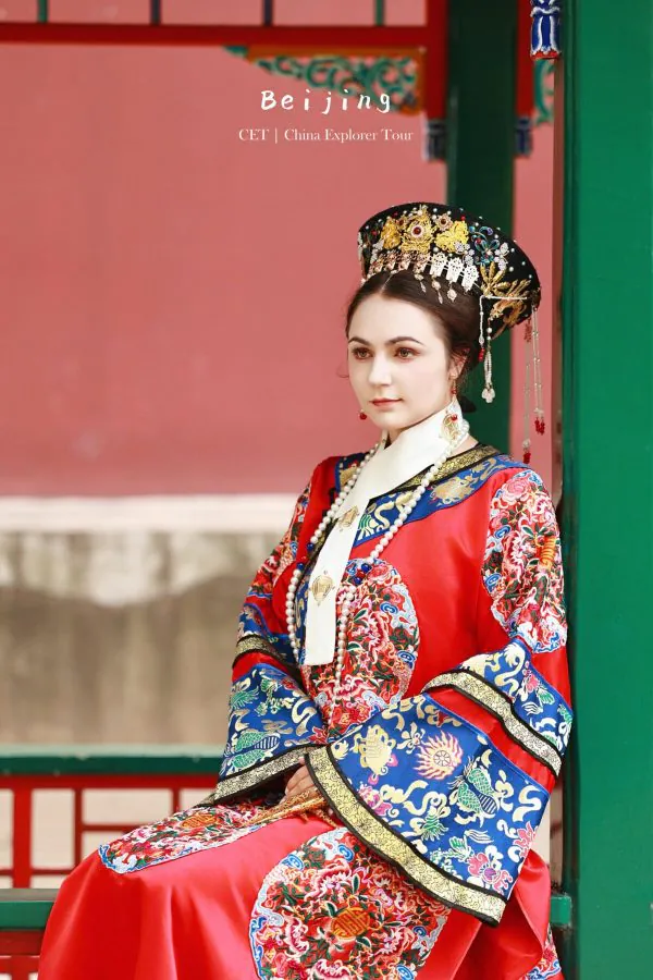 Hanfu photoshoot, zhongshan park, beijing, chinatravel, Woman wearing an ornate traditional Chinese imperial costume and headdress, seated beside a green pillar against a pink backdrop.