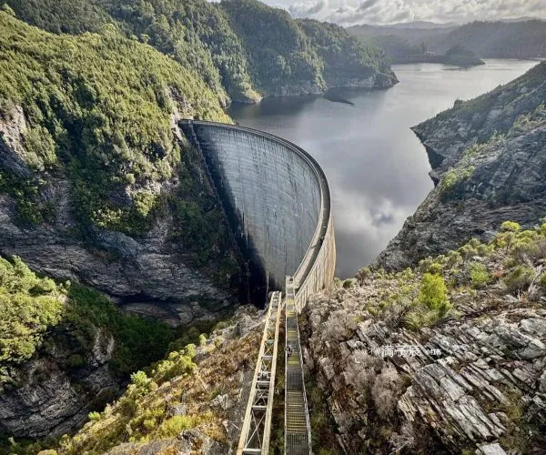 Three Gorges Dam Site,Yichang,Chinatravel Curved concrete dam spillway cutting through a rocky canyon with a calm reservoir and forested hills in the background.