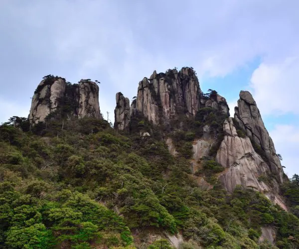 Sanqing Mountain Scenic Area,Shangrao,Chinatrip Towering granite peaks rising above a forested mountainside under a blue sky.
