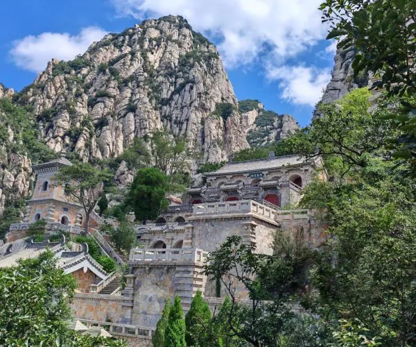 Sanhuangzhai,Shaolin & Songshan Area,Chinatrip Stone temple complex built into rugged mountain cliffs, with terraces, arches, and green trees against a blue sky.