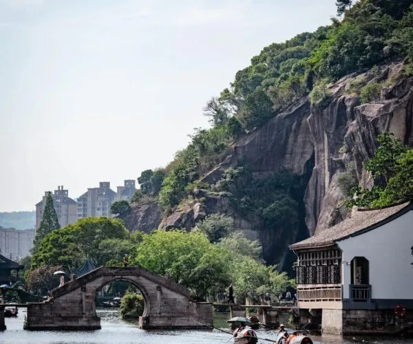 East Lake,Shaoxing,Chinatravel A tranquil water scene with a stone arched bridge, rowboats on the lake, and a traditional white building by a rocky, tree-covered hillside.