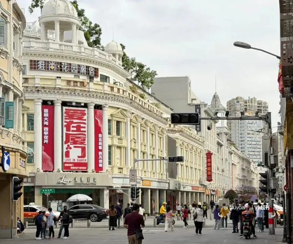 Zhongshan Road Pedestrian Street,Xiamen,Chinatravel Wide city street with white neoclassical buildings, red banners, and pedestrians crossing near shops.