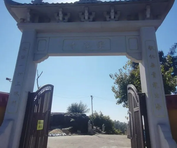 Yungu Temple,Huangshan,Chinatravel Ornate stone Chinese ceremonial arch (paifang) with dragon motifs, open double gates, sun behind, leading to a courtyard area.