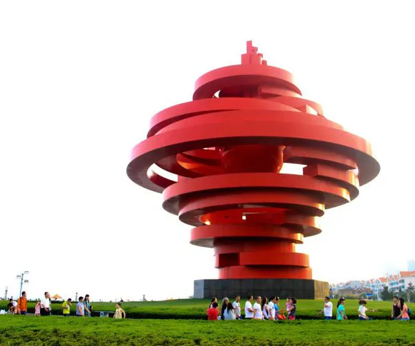 May Fourth Square,Qingdao,Chinatravel Large red spiraling sculpture in a park with groups of people at its base and city buildings in the background.