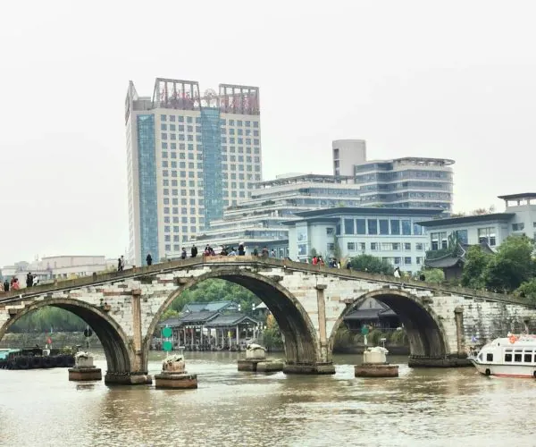 Grand Canal of China,Suzhou,Chinatravel Stone arched bridge over a river with pedestrians, modern buildings in the background says city skyline