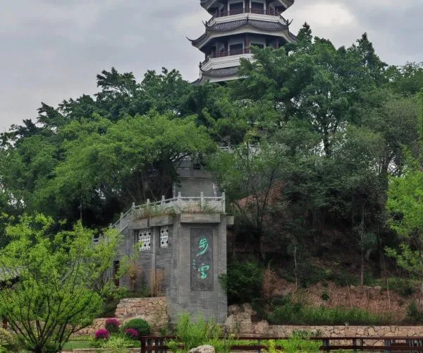 Lingyun Mountain National Forest Park,Leshan,Chinatravel Five-tier Chinese pagoda atop a hillside surrounded by trees, with a stone monument and garden in the foreground.