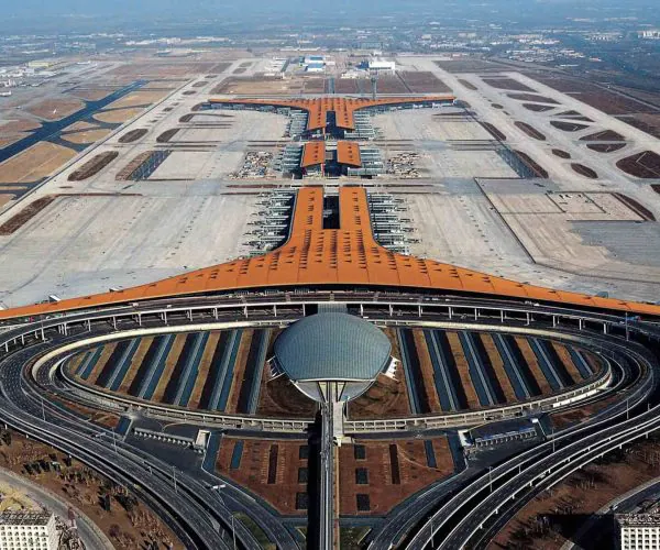 Beijing Capital International Airport, beijing, chinatravel, Aerial view of a large airport terminal with an orange roof and a central spine, surrounded by circular roadways and concourses.